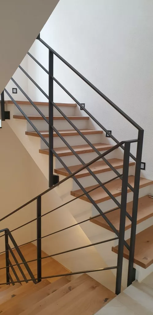 Geländer an Betontreppe in Burghausen. Pulverbeschichtetes Treppengeländer mit Stehern und Zwischengurten aus Flacheisen.