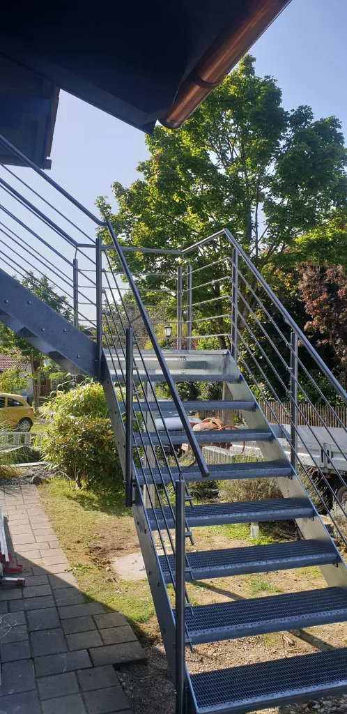 Treppenaufgang zum Balkon. Verzinkte Metalltreppe mit Gitterroststufen und Geländer aus Edelstahl-Rundprofilen.