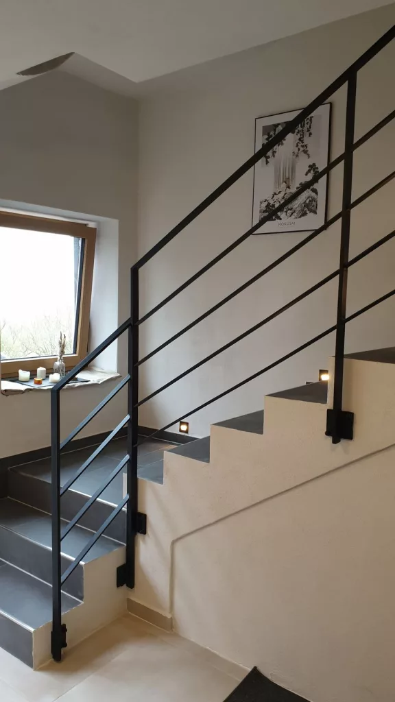 Metallgeländer mit Flacheisen als Gurte, Stehern und Handlauf, seitlich an eine Betontreppe montiert.